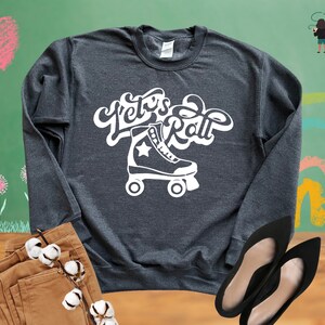 May include: A dark gray sweatshirt with the text "Let's Roll" in white, featuring a white roller skate with a star on the side.