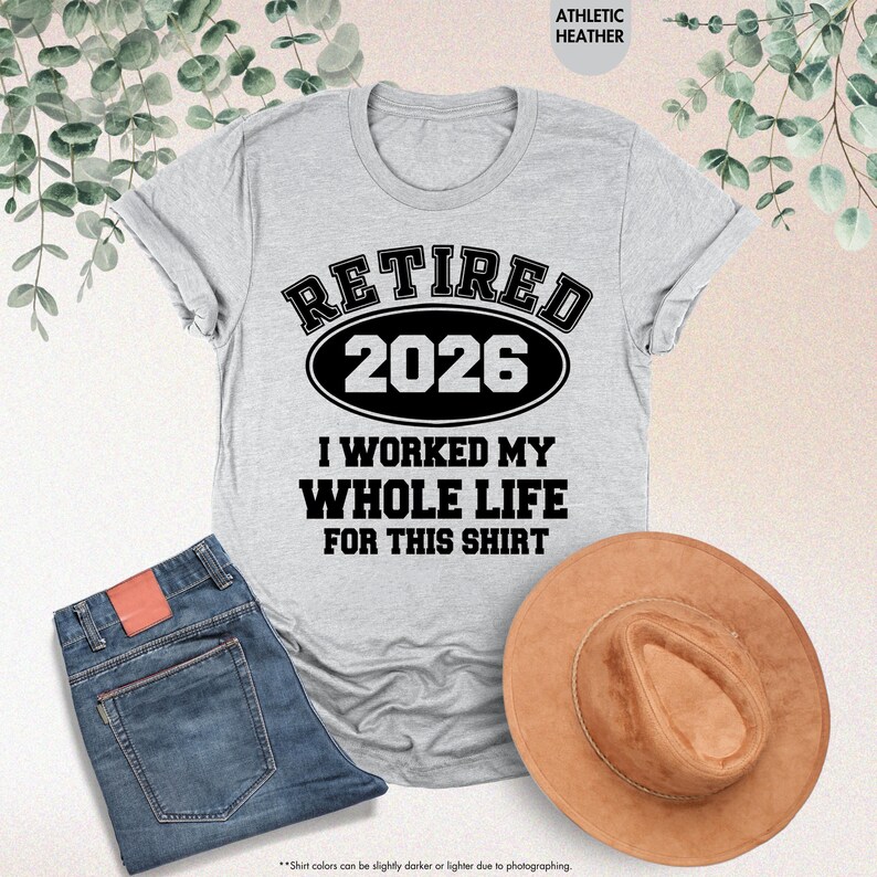Puede incluir: Camiseta gris atl&eacute;tica con el texto "RETIRED 2026 I WORKED MY WHOLE LIFE FOR THIS SHIRT" en negro. La camiseta se combina con vaqueros azules y un sombrero marr&oacute;n. Un atuendo informal.