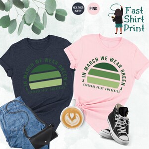May include: Two t-shirts with a green sunset graphic and the text "In March We Wear Green" and "Cerebral Palsy Awareness". One shirt is heather navy and the other is pink.
