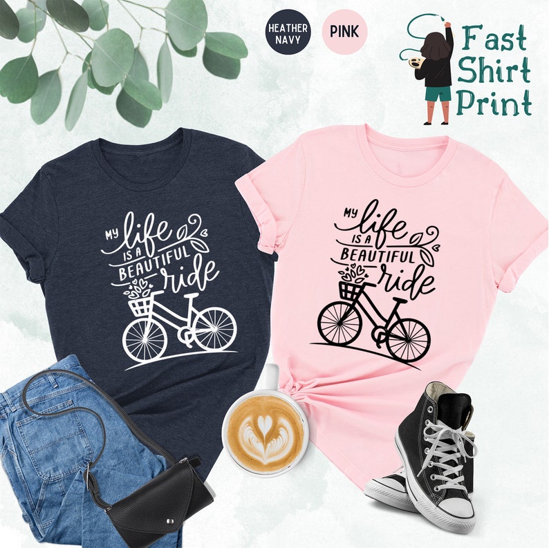 May include: Two t-shirts with a bicycle graphic and the text "My life is a beautiful ride". The t-shirts are in heather navy and pink.