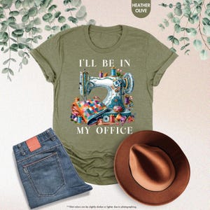 Pode incluir: Uma camiseta verde com o texto "I'll be in my office" e uma ilustra&ccedil;&atilde;o colorida de uma m&aacute;quina de costura com carret&eacute;is de linha e tecido.