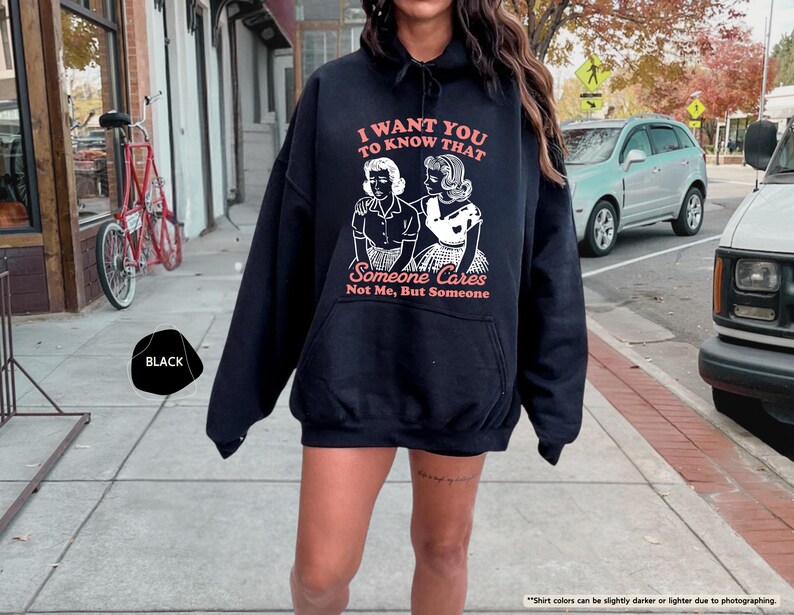 May include: Black hoodie with the text "I WANT YOU TO KNOW THAT Someone Cares Not Me, But Someone" in a retro font. The graphic features two women in vintage attire. The hoodie is a casual, oversized style.
