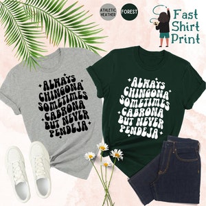 Puede incluir: Dos camisetas con el texto "Always Chingona Sometimes Cabrona But Never Pendeja" en una fuente retro. Las camisetas son de color gris jaspeado deportivo y verde bosque.
