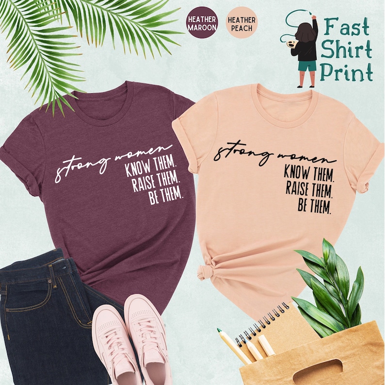 K&ouml;nnte beinhalten: Zwei T-Shirts mit dem Text "strong women know them. raise them. be them." bedruckt. Die Shirts sind in den Farben Heidelbeer-Melange und Pfirsich-Melange.