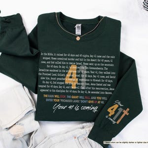 May include: A dark green sweatshirt with a white print that includes a Bible verse and the text "Your 41 is coming". The print also includes a graphic of a cross with the number 411.