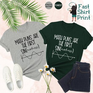 May include: Two t-shirts with a math pun design. The shirts are gray and green. The design says "Math puns are the first sin(madness)" with a graph of a sine wave.