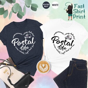 May include: Two t-shirts, one heather navy and one white, with a graphic design of a postal truck and the text "compassionate, caring, dedicated, Postal Life, warm, reliable, loyal, kind, fun".