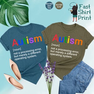 May include: Two t-shirts with the word "Autism" printed in rainbow colors. The text below the word defines autism as "not a processing error, but merely a different operating system."