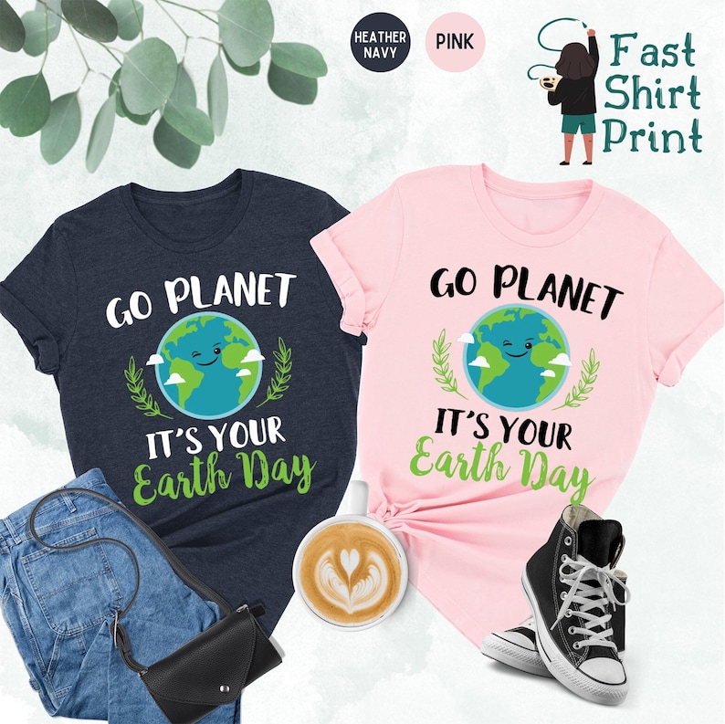 May include: Two t-shirts with the text "Go Planet It's Your Earth Day" printed on them. The shirts are in heather navy and pink colors. The graphic features a cartoon earth with a smiling face.