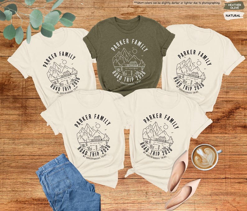 May include: Five t-shirts with a family road trip design. The shirts are in natural and olive green colours. The design includes the text "PARKER FAMILY ROAD TRIP 2026" with a mountain and lake graphic. A pair of jeans, shoes, and a coffee cup are also in the image.