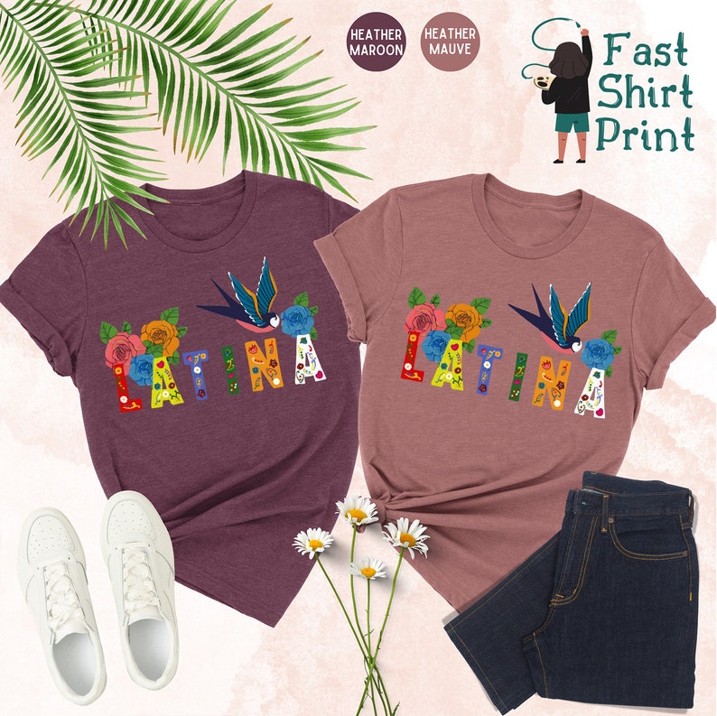 May include: Two t-shirts with the word "LATINA" in colorful letters decorated with flowers and a bird. The shirts are available in heather maroon and heather mauve.