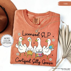 May include: A yam-coloured t-shirt with the text "Licensed SLP Certified Silly Goose." The shirt features four cartoon geese holding various tools and accessories. The shirt has a crew neck and short sleeves.