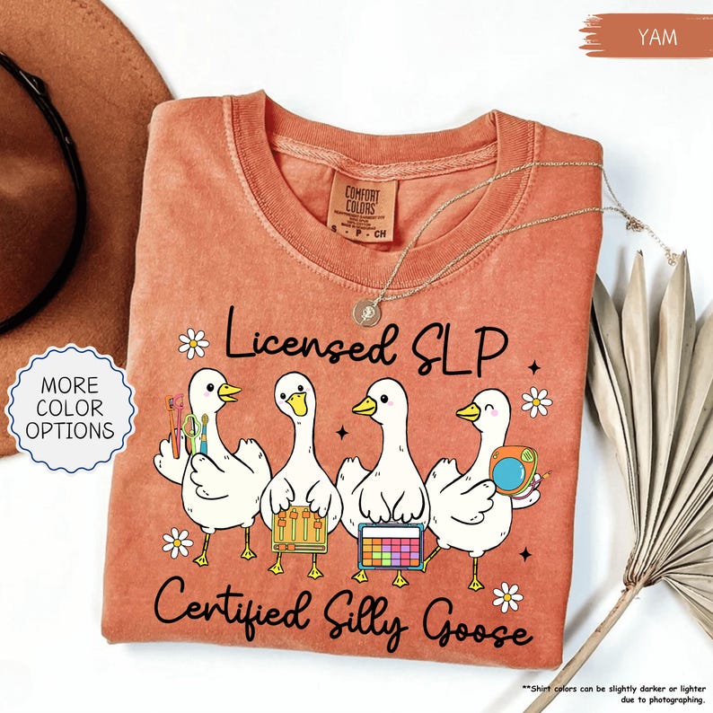 May include: A yam-coloured t-shirt with the text "Licensed SLP Certified Silly Goose." The shirt features four cartoon geese holding various tools and accessories. The shirt has a crew neck and short sleeves.