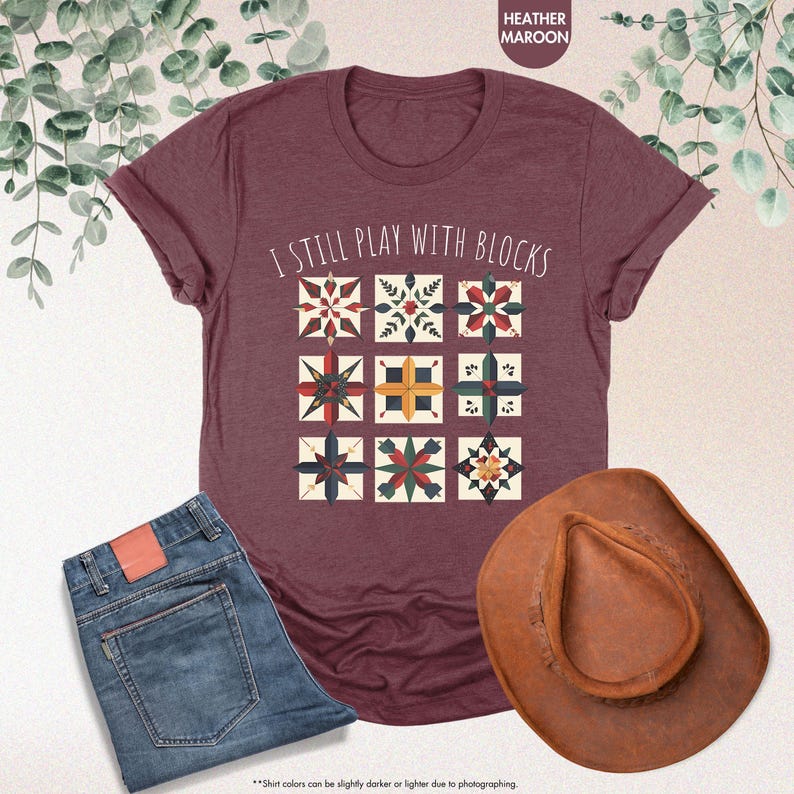 May include: A heather maroon t-shirt with the text "I still play with blocks" and a graphic of colorful quilt blocks.