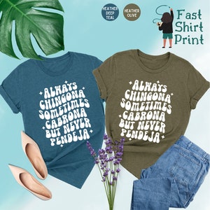 Puede incluir: Dos camisetas con el texto "Always Chingona Sometimes Cabrona But Never Pendeja" en una fuente retro. Las camisetas son de color azul oscuro jaspeado y verde oliva jaspeado.