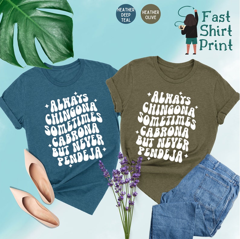 Puede incluir: Dos camisetas con el texto "Always Chingona Sometimes Cabrona But Never Pendeja" en una fuente retro. Las camisetas son de color azul oscuro jaspeado y verde oliva jaspeado.