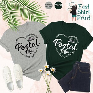 May include: Two t-shirts with a postal truck graphic and the text "Postal Life" in a circle. The text around the circle says "compassionate, caring, dedicated, warm, reliable, loyal, kind, fun". One shirt is grey and the other is green.