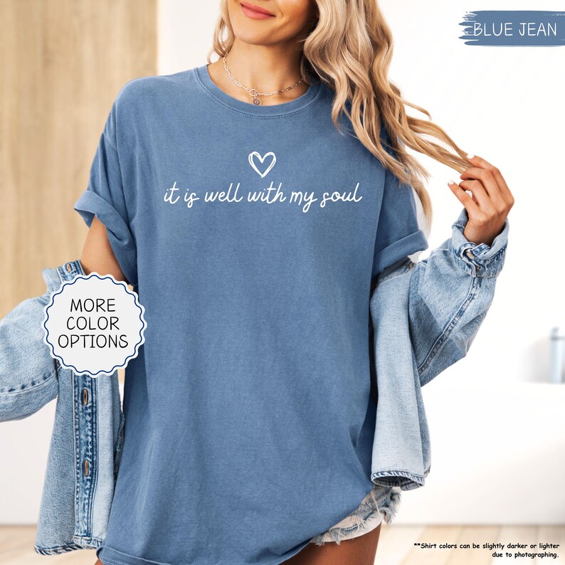 K&ouml;nnte beinhalten: Blaues Jeans-T-Shirt mit dem Schriftzug "it is well with my soul" in wei&szlig;er Schrift, &uuml;ber einem kleinen Herzen. Das Shirt hat hochgekrempelte &Auml;rmel und ist Teil einer Kollektion mit mehr Farboptionen.