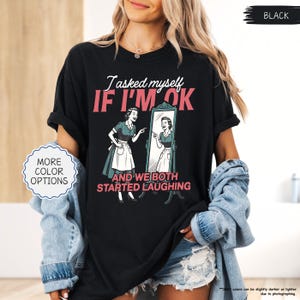 May include: Black t-shirt with the text "I asked myself IF I'M OK" and a retro illustration of a woman looking in a mirror. The graphic also includes the phrase "AND WE BOTH STARTED LAUGHING".
