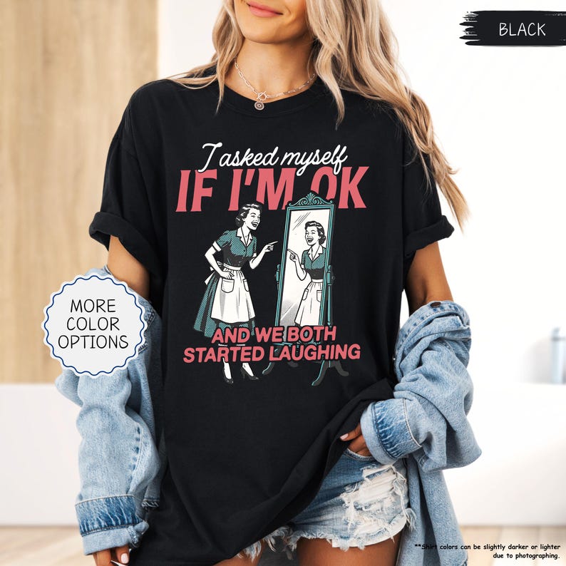 May include: Black t-shirt with the text "I asked myself IF I'M OK" and a retro illustration of a woman looking in a mirror. The graphic also includes the phrase "AND WE BOTH STARTED LAUGHING".