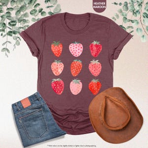 May include: A heather maroon t-shirt with a graphic of nine red and pink strawberries. The strawberries are arranged in a 3x3 grid.