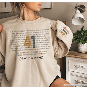 May include: A beige sweatshirt with a long-sleeve design featuring a text-based graphic with the words "Your 41 is coming" and a smaller graphic with the words "Your 41 is coming".