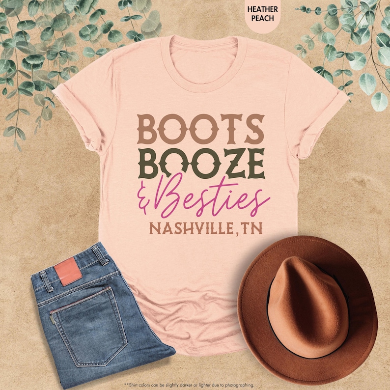 Pu&ograve; includere: Una maglietta color pesca con le parole "BOOTS, BOOZE, & Besties, NASHVILLE, TN" in lettere marroni e viola. La maglietta &egrave; abbinata a jeans blu e un cappello marrone.