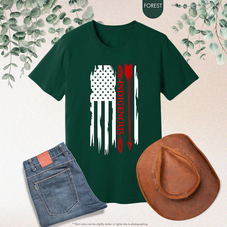 May include: A dark green t-shirt with a distressed American flag design and the word "INDIGENOUS" in red lettering. The flag is overlaid with a red arrow.