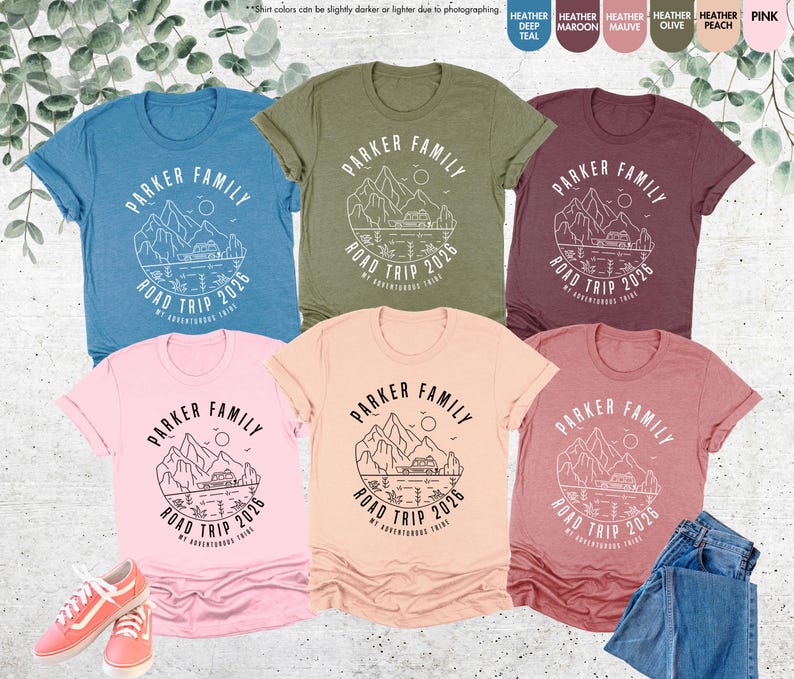 May include: A collection of t-shirts in various colours, including blue, green, pink, peach, and maroon. Each shirt features a mountain and camper graphic with the text "PARKER FAMILY ROAD TRIP 2026 MY ADVENTUROUS TRIBE."