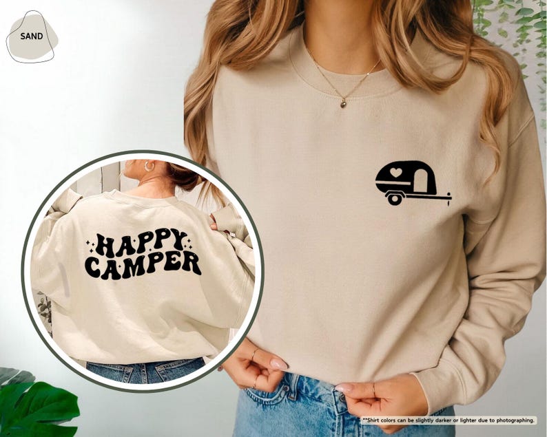 May include: Sand-colored sweatshirt with a black camper graphic on the front and the words "HAPPY CAMPER" on the back. The camper graphic includes a heart. The sweatshirt is a neutral color and suitable for casual wear.