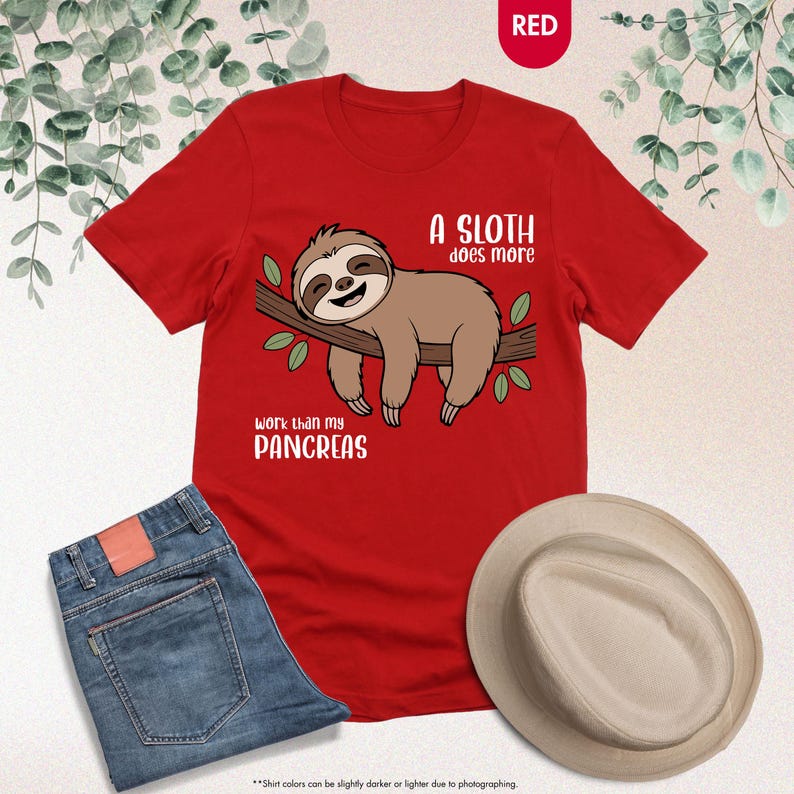 K&ouml;nnte beinhalten: Ein rotes T-Shirt mit einem Faultier-Motiv und dem Text "A sloth does more work than my pancreas." Das Faultier ist braun und liegt auf einem Ast. Das Bild zeigt auch eine blaue Jeans und einen beigen Hut.