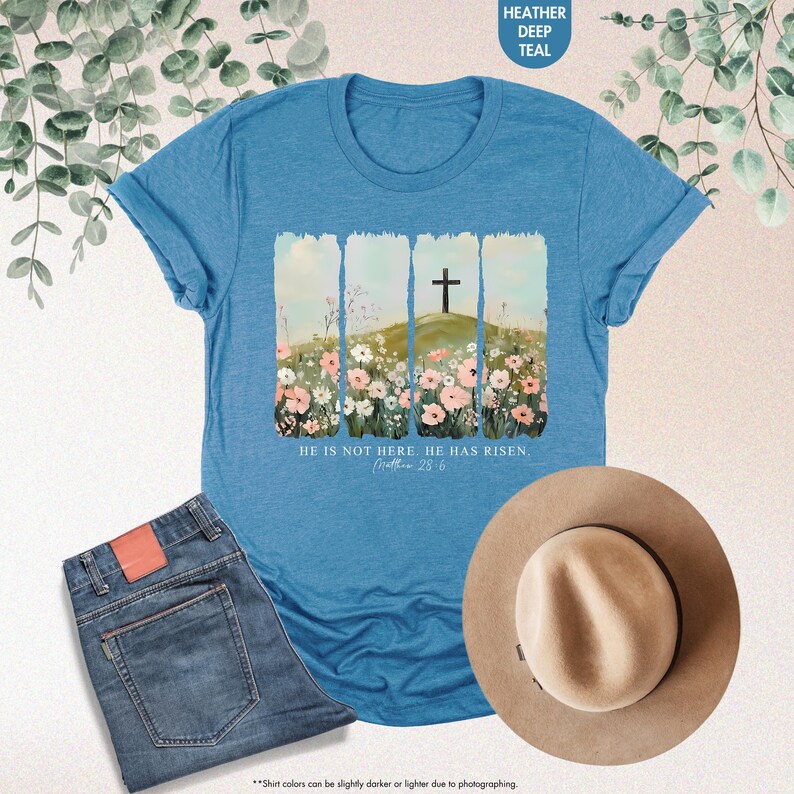 May include: A blue t-shirt with a floral design and a cross on a hill. The text "He is not here. He has risen. Matthew 28:6" is printed on the shirt.