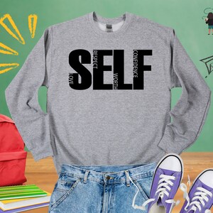 May include: Gray sweatshirt with the word "SELF" in black letters. The letters are made up of the words "respect", "love", "confidence", and "worth".