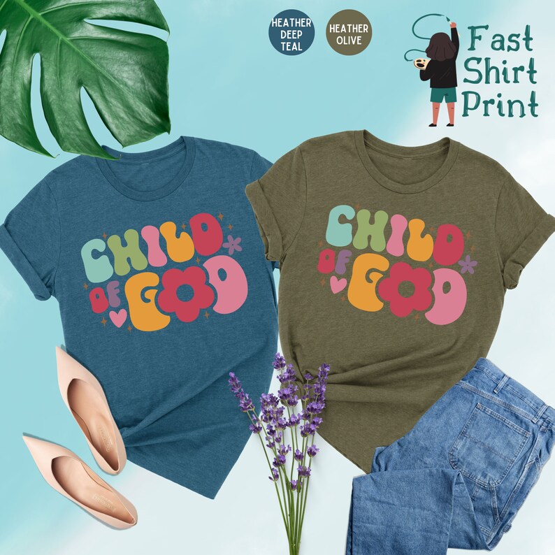 Op de afbeelding: Twee T-shirts met de tekst "Child of God" in een retro, kleurrijk lettertype. De shirts zijn in de kleuren heideblauw en olijfgroen.