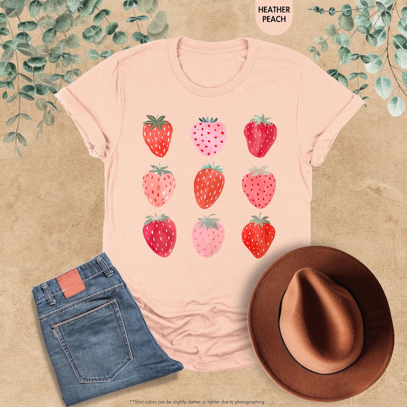 May include: A heather peach t-shirt with a graphic of nine red and pink strawberries. The strawberries are arranged in a 3x3 grid.