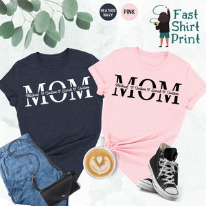 Puede incluir: Dos camisetas, una azul marino jaspeada y otra rosa, con la palabra "MOM" impresa en letras blancas grandes en la camiseta azul marino y en letras negras grandes en la camiseta rosa. La palabra "MOM" est&aacute; rodeada de un texto m&aacute;s peque&ntilde;o que dice "Michael Custom Sarah Custom".