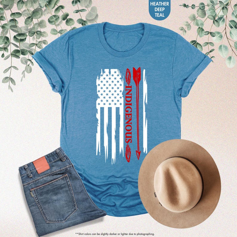 May include: A heather deep teal t-shirt with a white distressed American flag design. The flag has a red arrow with the word "INDIGENOUS" written vertically down the arrow.