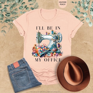 Pode incluir: Uma camiseta rosa com um gr&aacute;fico de uma m&aacute;quina de costura e o texto "Estarei no meu escrit&oacute;rio".