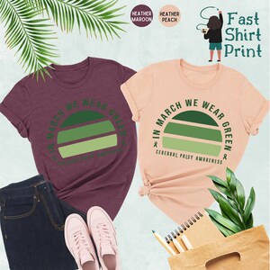 May include: Two t-shirts with a green sunset graphic and the text "In March We Wear Green & Cerebral Palsy Awareness". The shirts are available in heather maroon and heather peach.