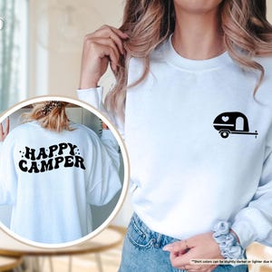 May include: White sweatshirt with a black camper graphic on the front and the words "HAPPY CAMPER" on the back. The camper graphic includes a heart. A casual, long-sleeved top for camping enthusiasts.