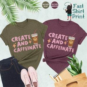 May include: Two t-shirts with the text "Create and Caffeinate" in pink letters, a coffee cup with a smiley face, and sparkling stars. The t-shirts are in heather olive and heather maroon.