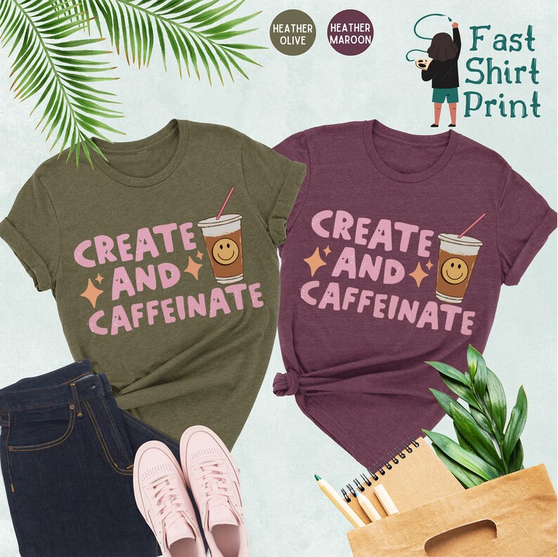 May include: Two t-shirts with the text "Create and Caffeinate" in pink letters, a coffee cup with a smiley face, and sparkling stars. The t-shirts are in heather olive and heather maroon.
