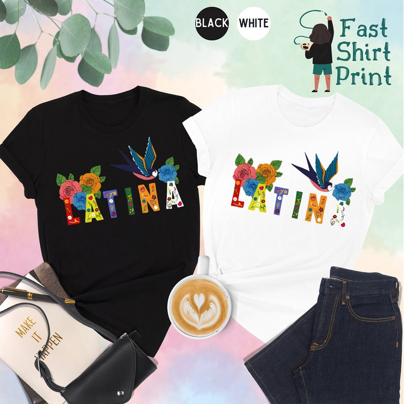May include: Two t-shirts, one black and one white, with the word "LATINA" and "LATIN" printed on them in colorful letters decorated with flowers and a bird. The shirts are displayed on a pink and white background with a cup of coffee, a book, and a purse.