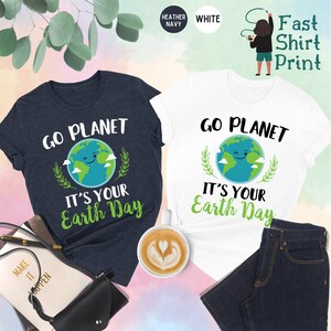 May include: Two t-shirts with a graphic of a smiling earth with clouds and leaves. The text on the shirts reads "Go Planet It's Your Earth Day". The shirts are available in heather navy and white.