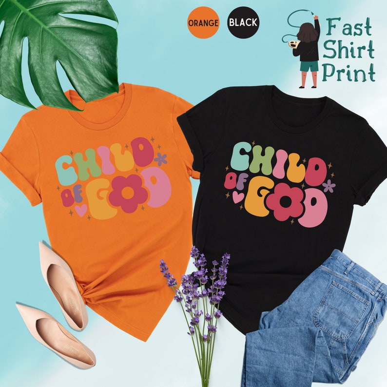 Op de afbeelding: Twee T-shirts met de tekst "Child of God" in kleurrijke, retro-stijl letters. Een shirt is oranje en de andere is zwart.