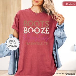 Pu&ograve; includere: T-shirt color cremisi con le parole "BOOTS BOOZE &ties" in un design a strati. Il testo "NASHVILLE, TN" &egrave; in basso. La maglietta ha una vestibilit&agrave; ampia e maniche arrotolate. Un bottone sul lato sinistro dice "MORE COLOR OPTIONS".