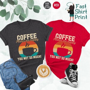 May include: Two t-shirts with a vintage-style graphic of a coffee cup and the text "Coffee Makes Me Happy You Not So Much!" One shirt is dark heather grey and the other is red.
