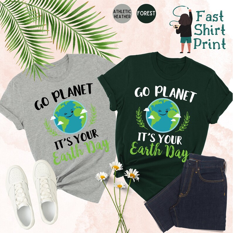 May include: Two t-shirts with a green and blue earth graphic and the text "Go Planet It's Your Earth Day". The shirts are on a white background with green leaves and white flowers.