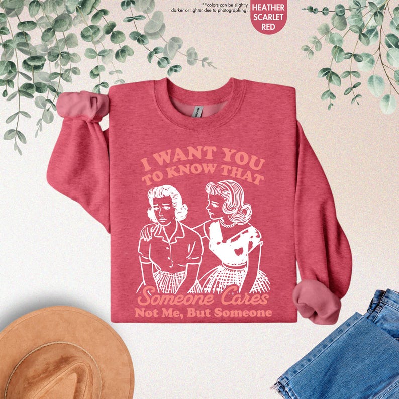 May include: Heather scarlet red sweatshirt with the text "I WANT YOU TO KNOW THAT Someone Cares Not Me, But Someone" and a graphic of two women. The long-sleeved top has a crew neck and a relaxed fit.