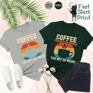 May include: Two t-shirts with a retro sunset design and a coffee cup. The text on the shirts reads "Coffee makes me happy, you not so much!"
